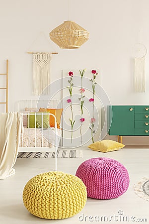 Yellow and pink pouf in the middle of boho female bedroom with green cabinet, flower board, single bed and macrame on the wall Stock Photo