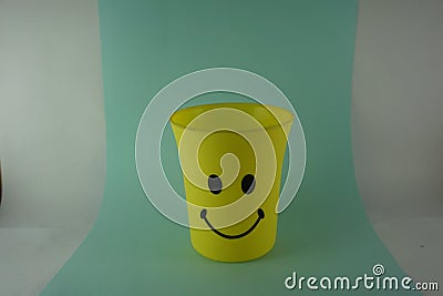 A yellow plastic cup with a smiling face, so it is very popular with children. Blue Background. Kids toys, kid friendly Stock Photo