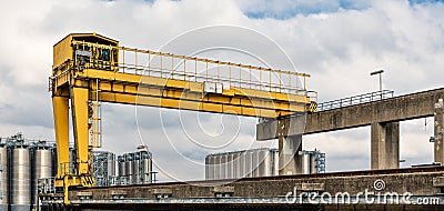 A yellow portal crane with a silo complex in the background Stock Photo