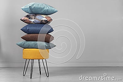 Yellow pouf on steel legs with pillows in a stack, on a gray background. Space for text Stock Photo
