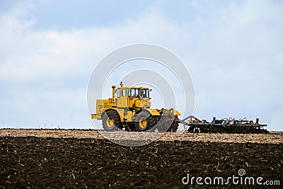 Yellow powerful wheeled tractor pulls the disc harrow Stock Photo