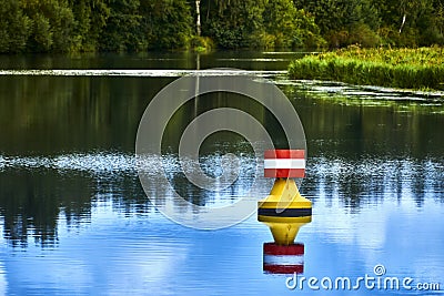 Yellow red buoy on a calm river to mark the shipping route in the upper reaches of a weir, reed belt in the background Stock Photo