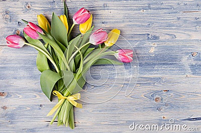 Yellow and red tulips bouquet with ribbon on blue shabby chic wood board. April spring easter background. Stock Photo