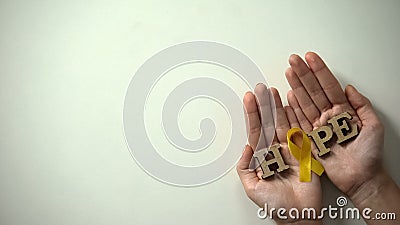 Yellow ribbon and hope word in hands, childhood cancer awareness, healthcare Stock Photo