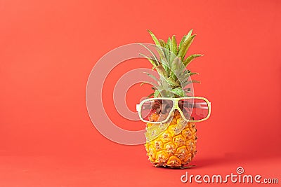 Yellow ripe pineapple in dark sunglasses on a red background. Funny face from a tropical fruit. Concept Copy space. Stock Photo