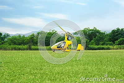 Yellow rotorcraft flying above grass near trees Stock Photo