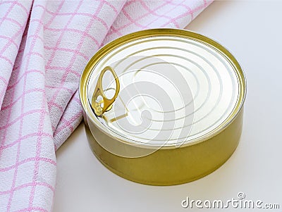 Yellow round tin can near checkered kitchen towel on a white table. Opening a food can with pull tab Stock Photo