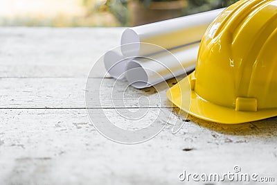 yellow safety helmet and rolled up architectural blueprints on a wooden desk Stock Photo