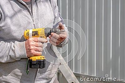 Yellow scratched cordless screwdriver in corpus callosum male hands. Sunny day Stock Photo