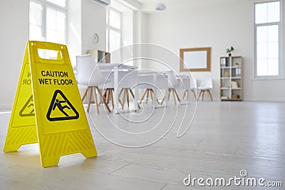 Yellow sign that reads Caution Wet Floor standing in clean empty school classroom Stock Photo