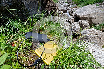 Yellow smartphone charged from a black external battery powerbank, placed on grass, near rocks, up in the mountain Stock Photo