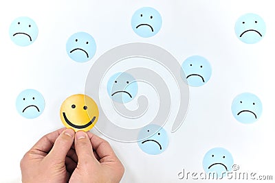 A yellow smiling face icon among a group of sad face emoticons. Positivity, attraction and happiness. Stock Photo