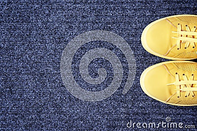 Yellow sneakers on gray doormat, top view. Stock Photo