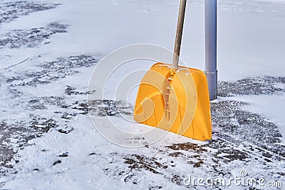 Yellow snow shovel leaning against a pole on a snowy pavement Stock Photo