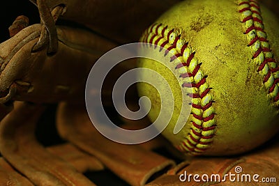 Yellow softball closeup with red seams on a brown leather glove. Stock Photo