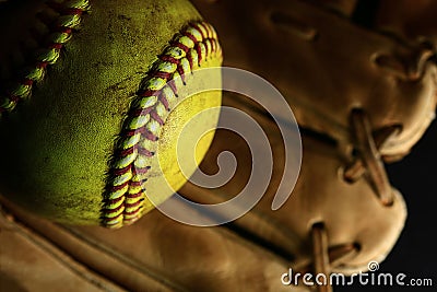 Yellow softball closeup with red seams on a brown leather glove. Stock Photo