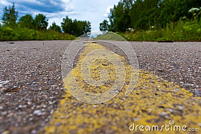 Yellow solid line, grunge road marking on asphalt close up with rural landscape on background Stock Photo