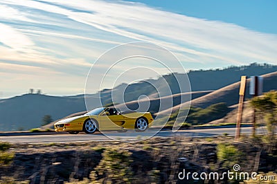 Yellow sports car traveling along a winding road with majestic mountains in the background. Editorial Stock Photo