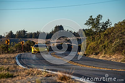 Yellow sports car traveling along a winding road with majestic mountains in the background. Editorial Stock Photo