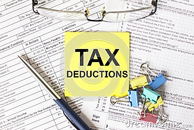 Yellow sticker with text Tax Deductions. Next to it is a blue pen with colored stationery clips and eyeglasses Stock Photo