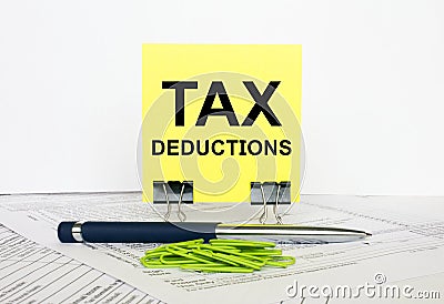 Yellow sticker with text Tax Deductions stands on office clips. Next to it is a blue pen with green paper clips Stock Photo