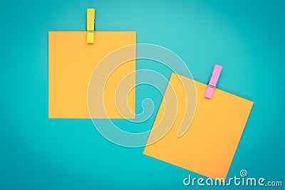 Yellow sticky note with clothespin. Two orange stickers on a blue bulletin board. Reminder, planning concept. Turquoise background Stock Photo