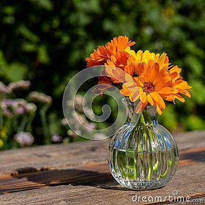 Yellow summer flowers in a glass vase on an old wooden surface. Calendula flowers. Orange calendula flowers in a glass vase. Stock Photo