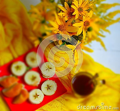 Yellow sunroot flowers, a treat on a red plate, a cup of tea on a yellow knitted blanket Stock Photo