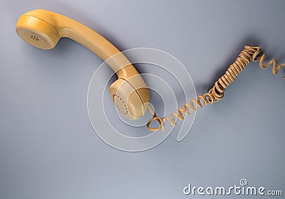 Yellow telephone receiver with twisted cord from an old antique rotary phone on blue background. Plastic removed handset Stock Photo