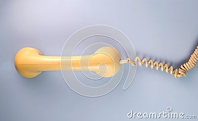 Yellow telephone receiver with twisted cord from an old antique rotary phone on blue background. Plastic removed handset Stock Photo