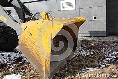 Yellow tractor knife on the ground against the background of a house in the city Stock Photo
