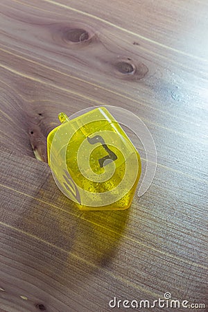 Yellow translucent plastic Hanukkah dreidel on a wood table, Hebrew letter Nun facing up Stock Photo