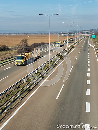Yellow transportation semi trucks in line on a countryside highway Stock Photo