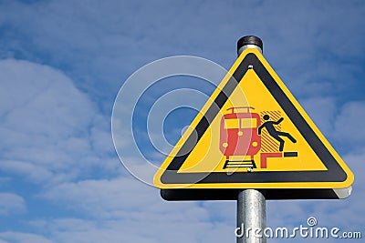 Yellow triangular warning sign for passengers on a platform meaning beware of incoming and passing trains Stock Photo