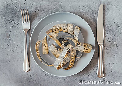 Yellow twisted measuring tape on a brown plate on a gray background, top view, knife, fork, dishes, diet, concept Stock Photo