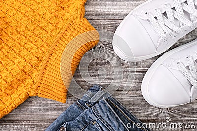 Yellow warm pullover for cold autumn, jeans denim and winter weather with white casual leather sneakers on wooden background Stock Photo