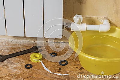 A yellow water basin and a set of tools near a leaking radiator. Accident of the heating system of a private house. Stock Photo