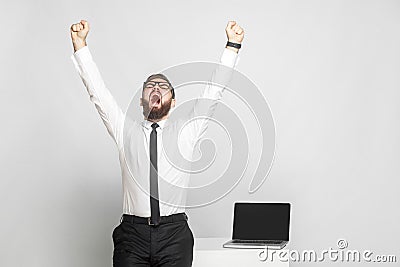 Yes! Happy screaming bearded young businessman in white shirt and black tie are standing near his working place are triumphing Stock Photo