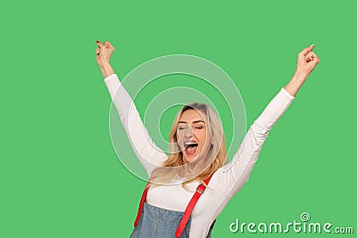 Yes I am winner! Portrait of enthusiastic adult woman in stylish denim overalls shouting hurray and keeping hands up Stock Photo