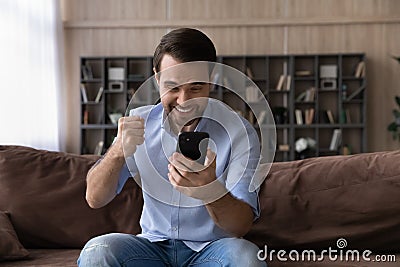 Amazed millennial guy student hold phone clench fist super great Stock Photo