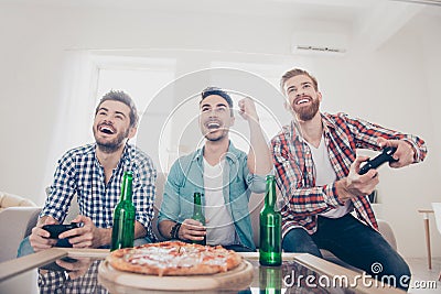 Yes! Team of winners! Bachelor men`s life. Low angle of three happy joyful men, sitting on sofa and playing video games with beer Stock Photo