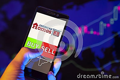 Company logo American Homes 4 Rent on smartphone screen, hand of trader holding mobile phone showing BUY or SELL on background of Editorial Stock Photo