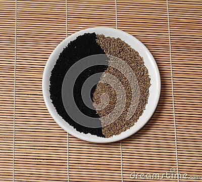 Yin Yang yellow seeds black cumin white plate bamboo Mat Stock Photo