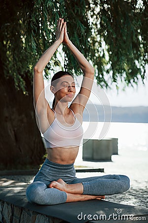 Yoga exersice. Girl in sportive clothes sits outdoors near the tree Stock Photo