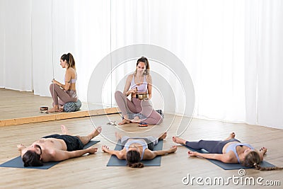 Yoga instructor and group of young sporty people in yoga studio, lying and relaxing on yoga mats during restorative yoga Stock Photo