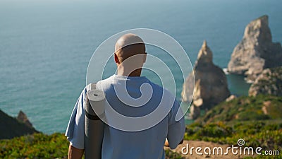 Yoga man walking edge cliff holding mat. Focused sportsman looking ocean coast Stock Photo