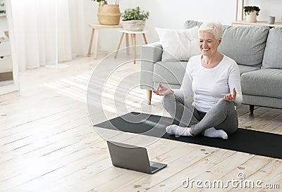 Yoga online. Relaxed senior woman meditating in front of laptop at home Stock Photo