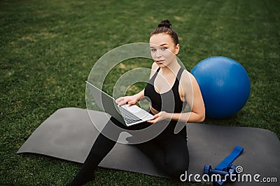 Yoga in the park with sunlight. A young girl in a lotus position sits on green grass holding a phone in her hand and watches Stock Photo