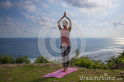 Yoga pose. Woman practicing yoga. Young woman raising arms with namaste mudra. Outdoor yoga on the cliff. Bali Stock Photo