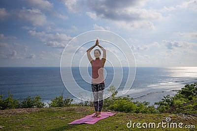 Yoga pose. Woman practicing yoga. Young woman raising arms with namaste mudra. Outdoor yoga on the cliff. Bali Stock Photo